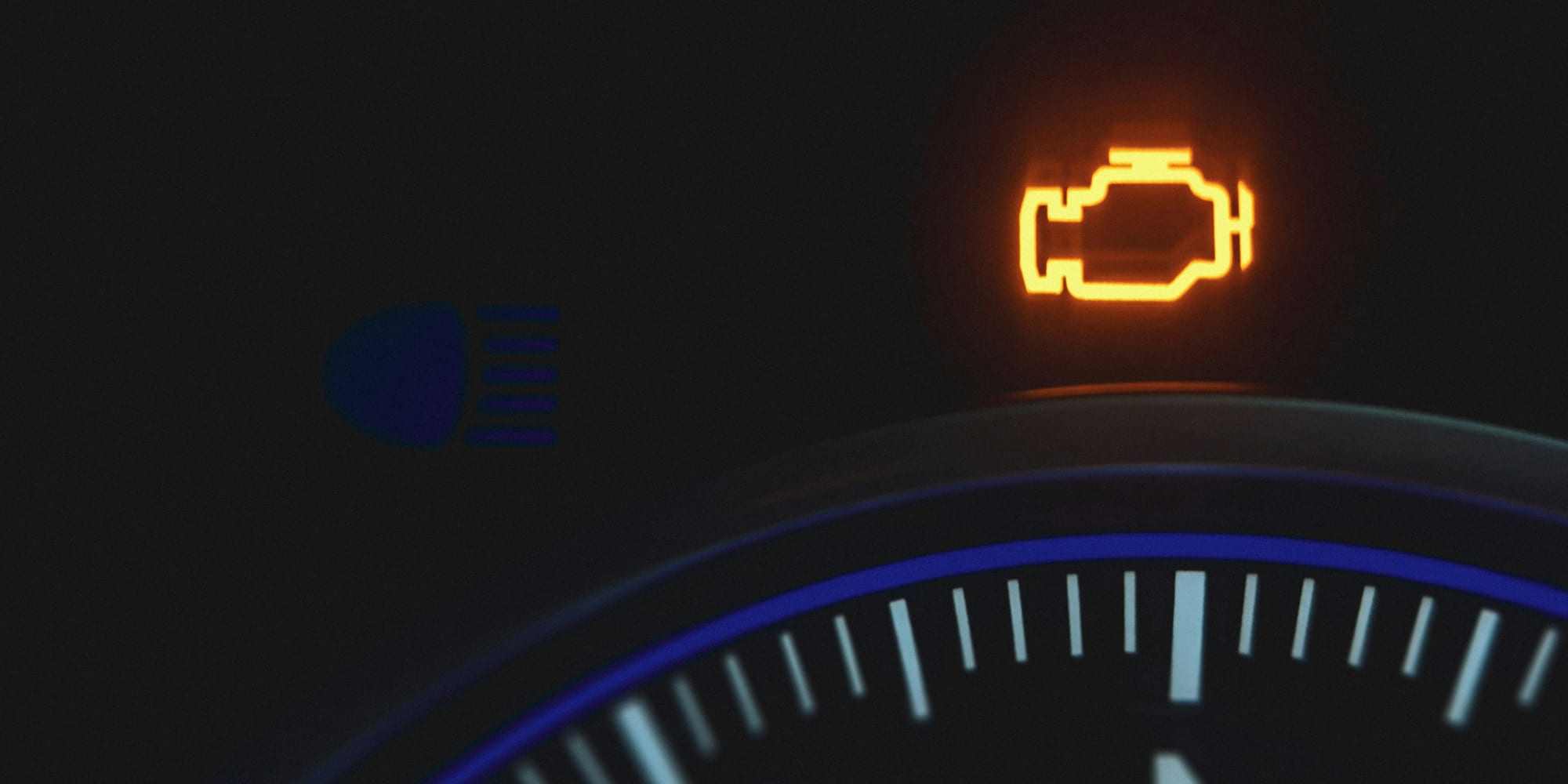 An amber check engine light glowing on a dark dashboard instrument cluster