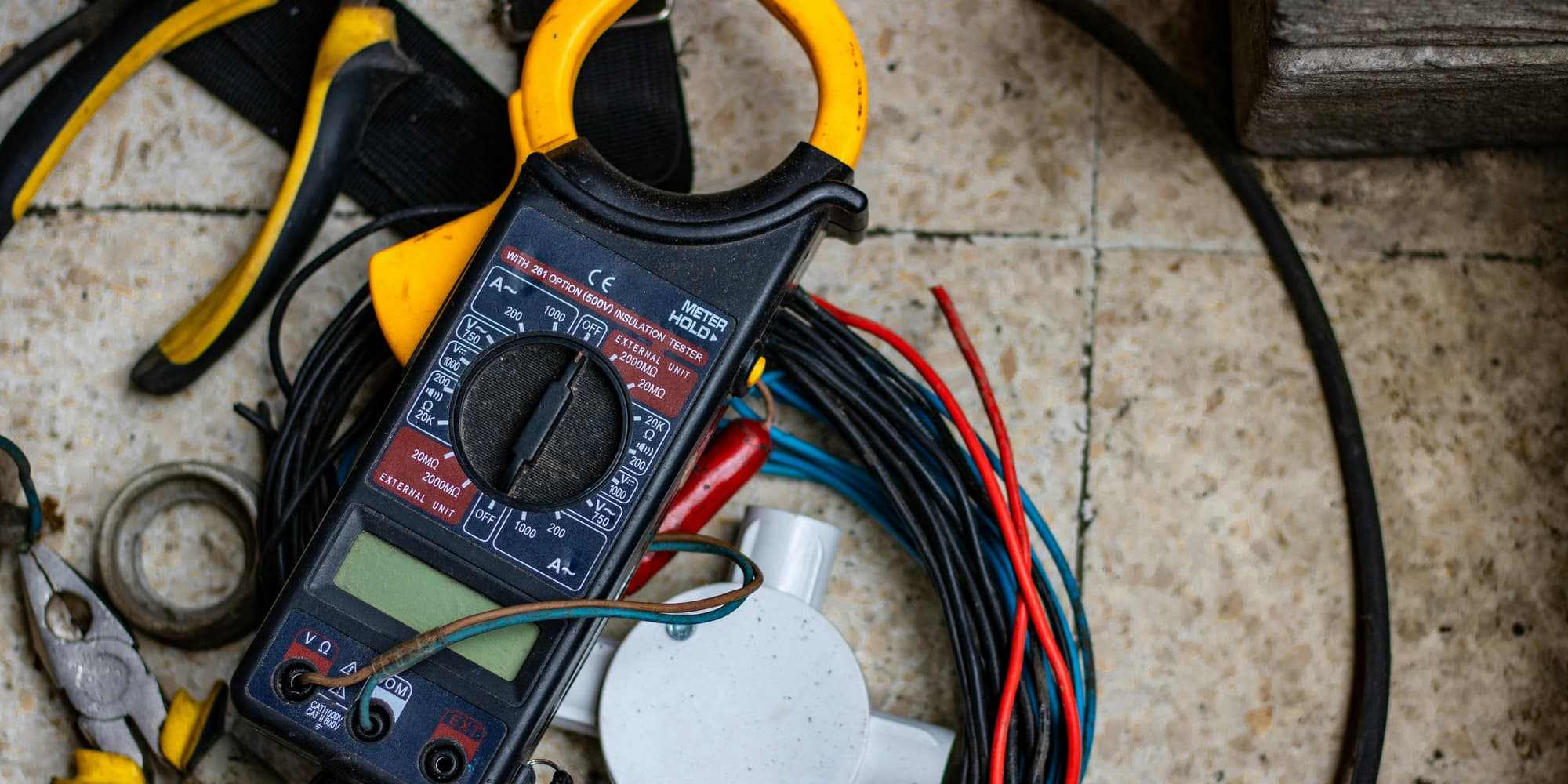 A clamp multimeter and a tangle of colored wires laid out on a shop floor during an electrical diagnosis
